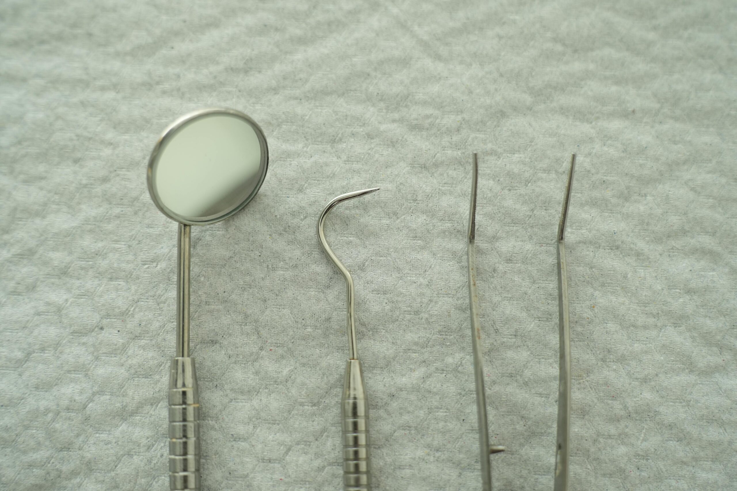Close-up of dental tools including mirror and pick on a gray textured background.